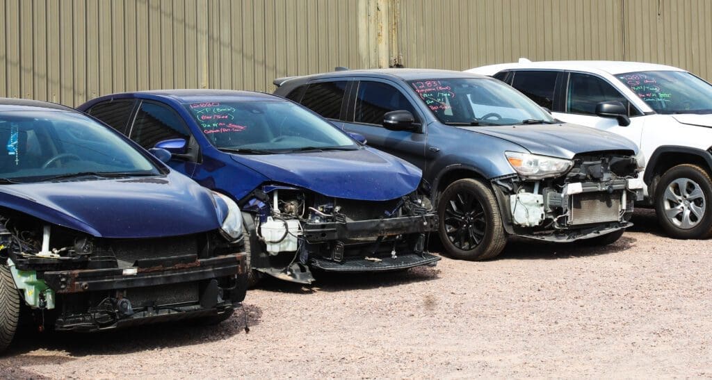 A row of damaged cars parked outdoors in a lot.