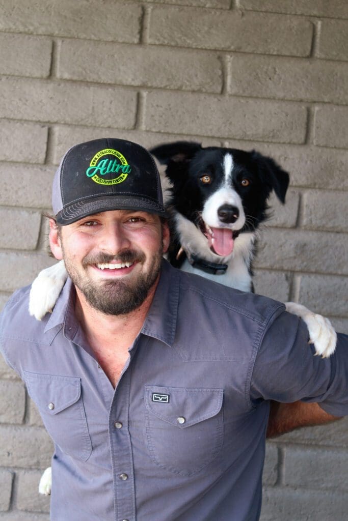 Man smiling with a black and white dog on his shoulder.