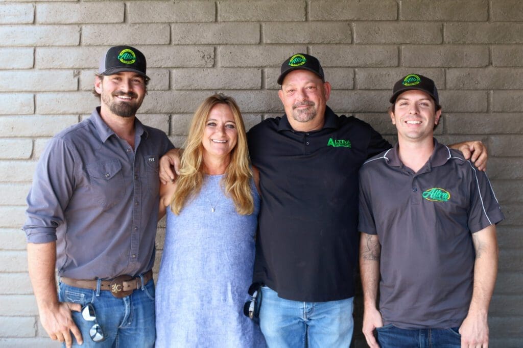 Four people smiling, standing in front of a brick wall.