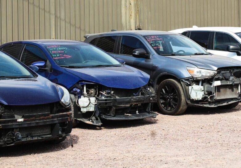 A row of damaged cars parked outdoors in a lot.