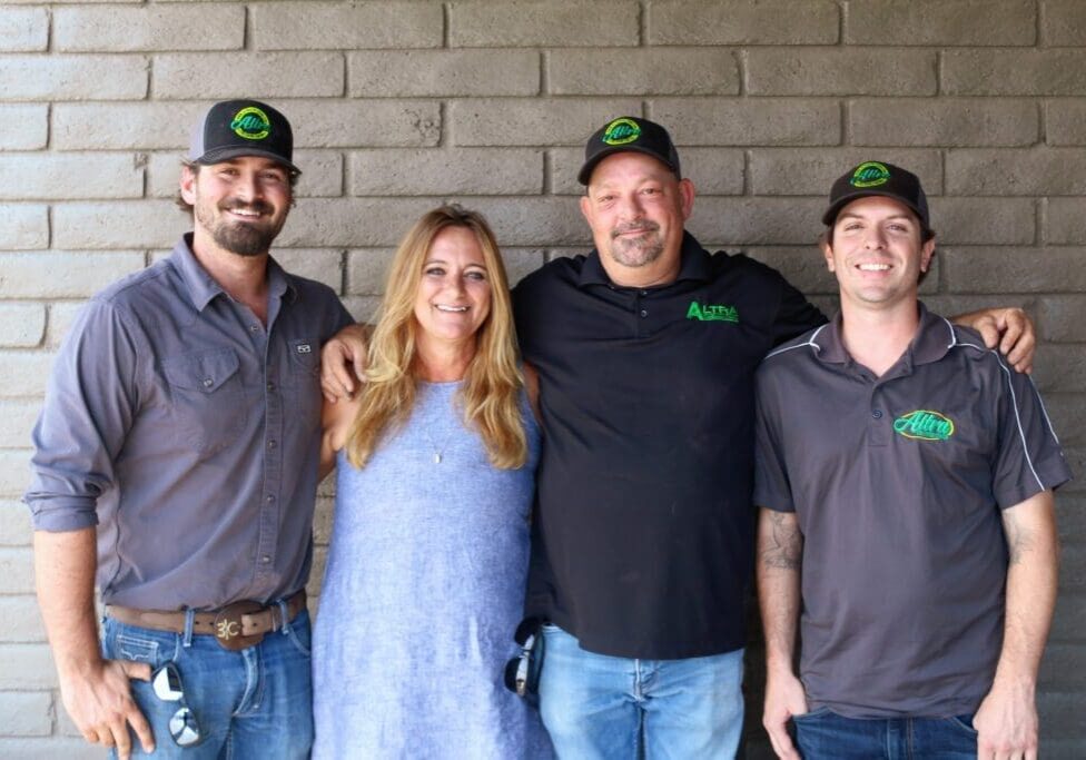 Four people smiling, standing in front of a brick wall.